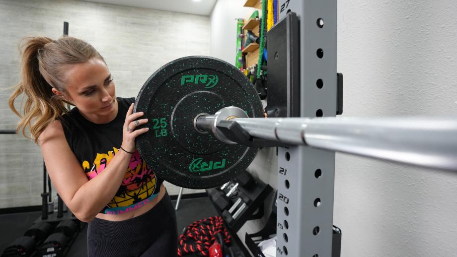 A woman can be seen pushing a weight plate onto the Living.Fit Barbell