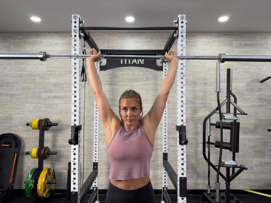 A woman performs an overhead press with the Living.Fit Barbell