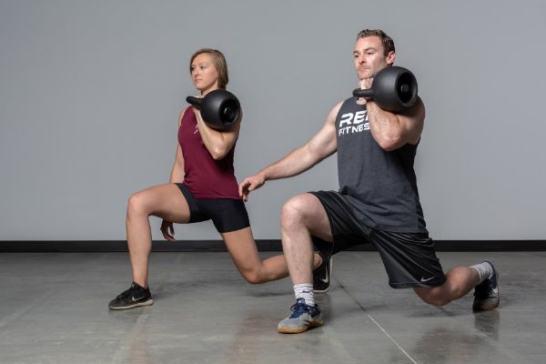 Man and woman lunging with REP Fitness Adjustable Kettlebells.