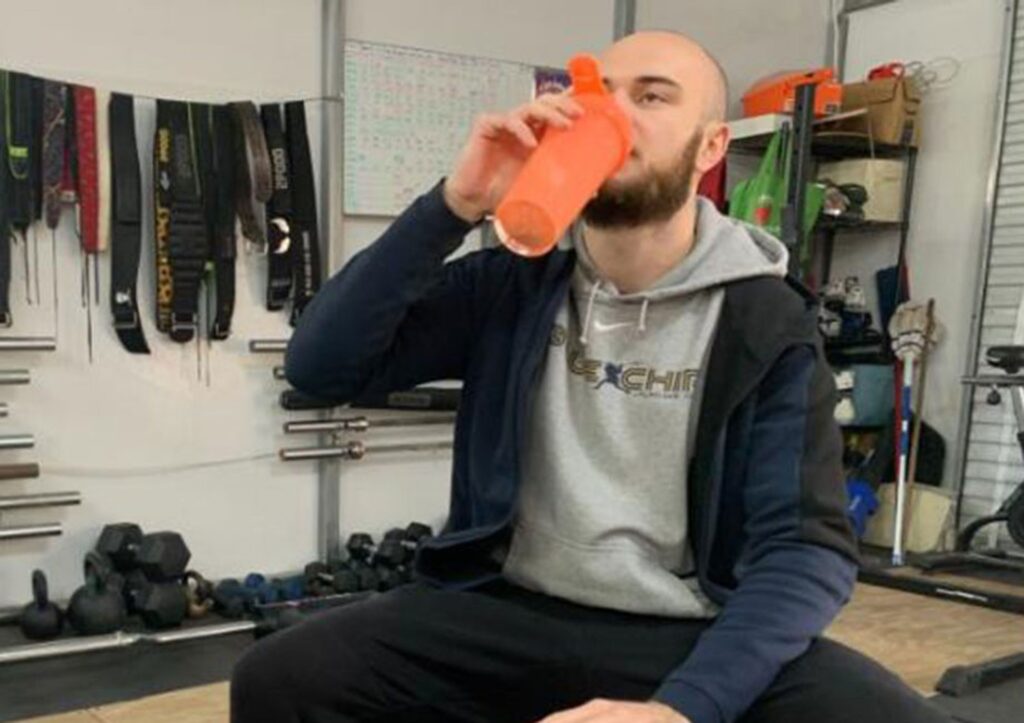 A man is shown drinking a Pre-Workout in a gym.