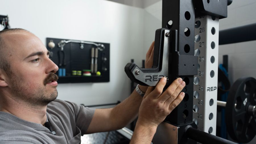 Man placing a j-cup rack attachment on a power rack