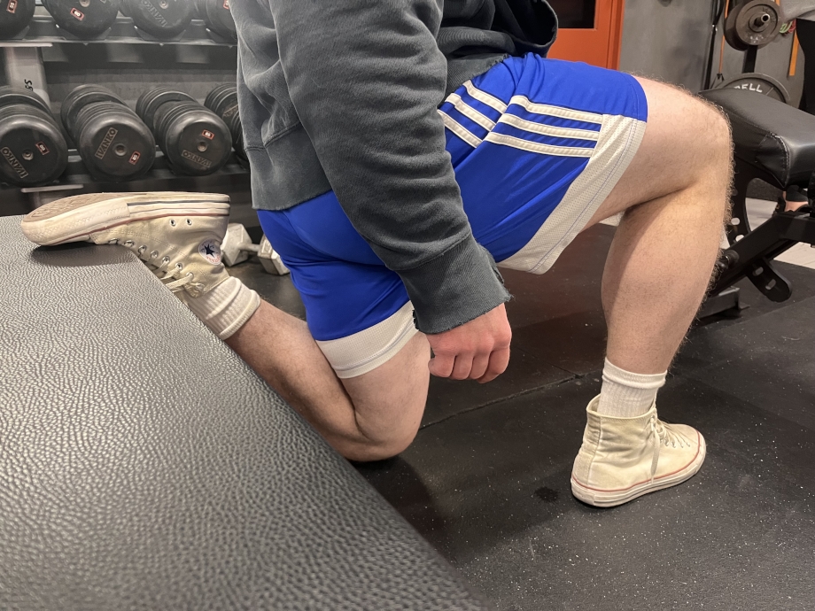 A man squats with a weight bench wearing Converse Chuck Taylor shoes. 