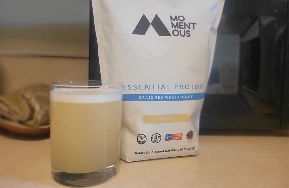 A close up view of a momentous whey shake in a glass next to the bag.