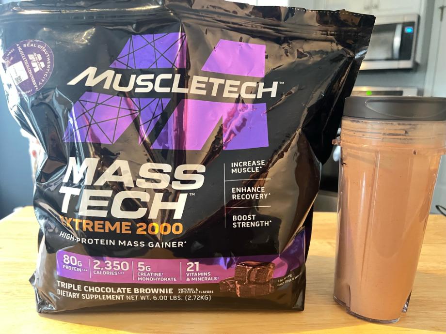 A full shaker cup sits prominently next to a bag of MuscleTech Mass Gainer.