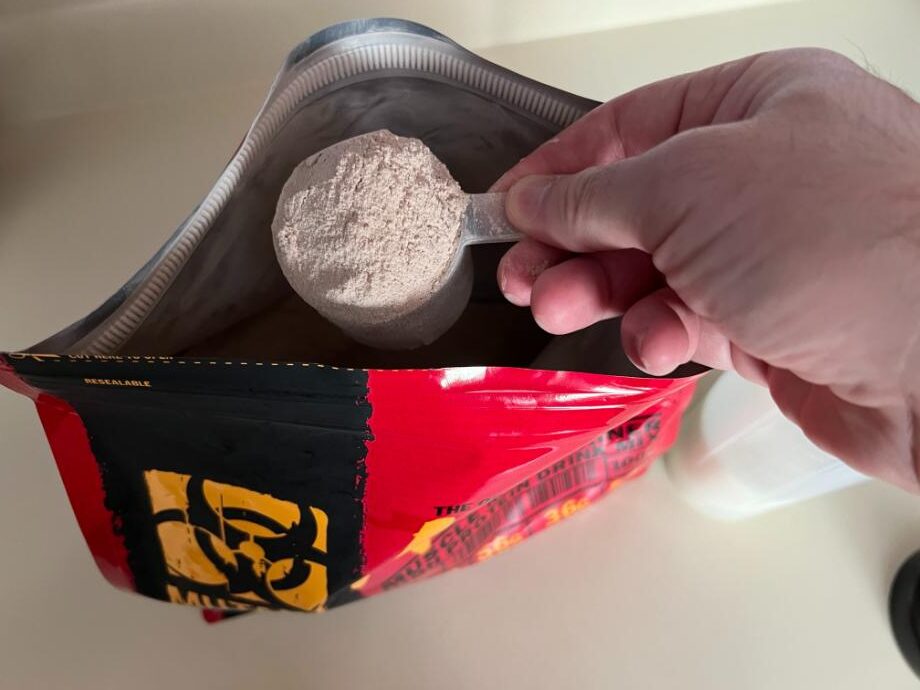 Looking down on a hand holding a scoop of Mutant Mass in the opening of the bag.