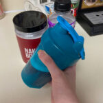 A hand holds a shaker bottle in front of a container of Naked BCAAs.