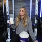 A woman smiles while holding up a shake made with Naked Nutrition Naked Mass gainer.