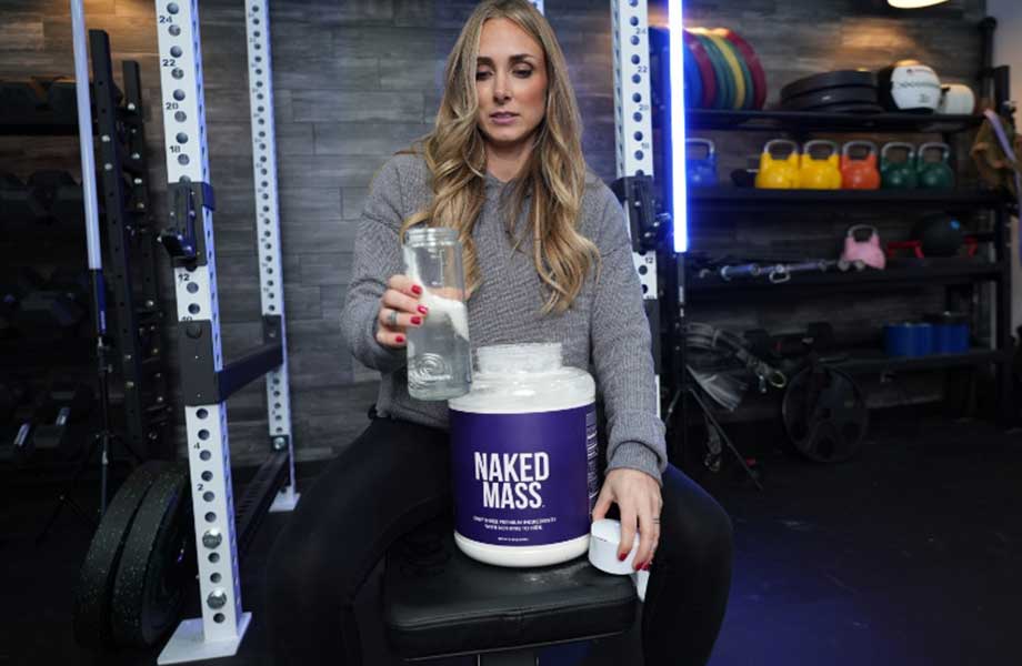 A woman holds up a shaker glass of water and mixes in some Naked Nutrition Naked Mass gainer.