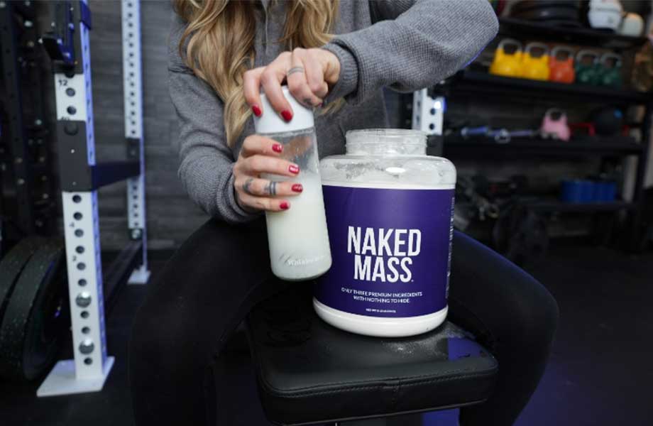 A woman is taking the lid off of a freshly mixed shake made from Naked Nutrition Naked Mass gainer.