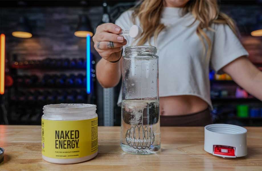 Woman dumping a scoop of Naked Pre-workout into a shaker bottle