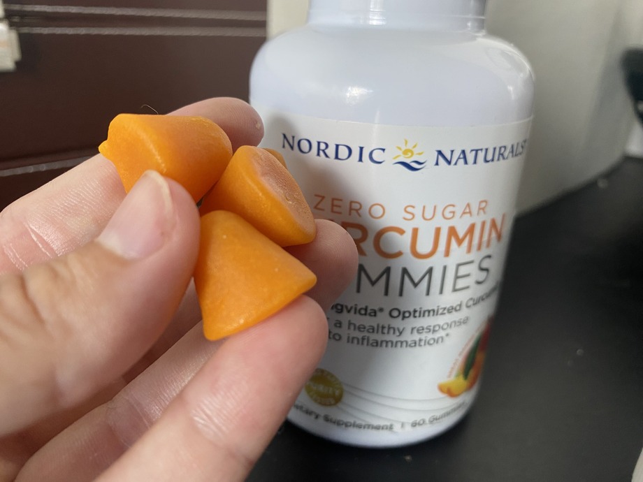 A hand holding Nordic Naturals Curcumin gummies next to the bottle