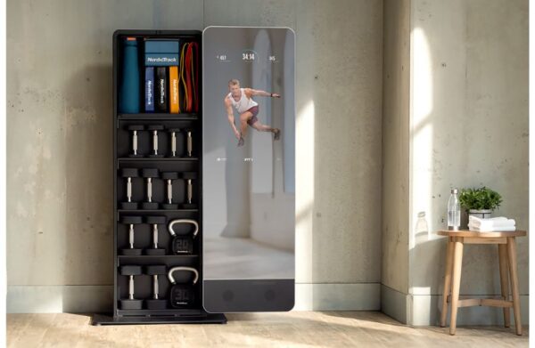 Product image of the NordicTrack Vault showing a workout on the reflective screen, with dumbbells and kettlebells stored on the attached shelving.