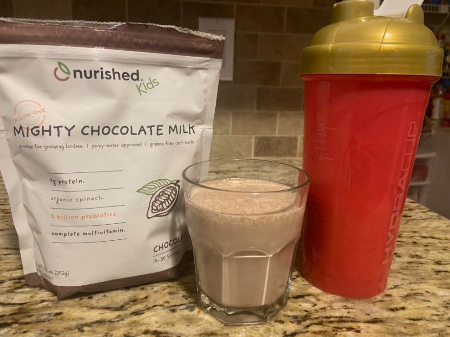 A bag of Nourished Kids protein powder with a glass and shaker bottle