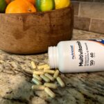 Close-up of open tipped-over bottle of Nutricost Multivitamins, with a handful of capsules filled with a yellowish powder spilling out.