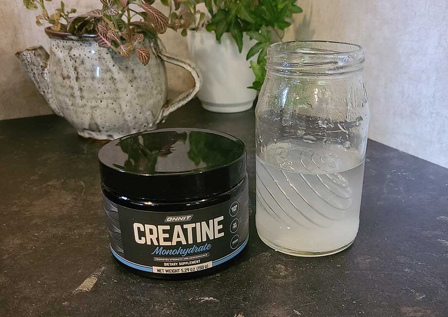 A container of Onnit Creatine next to a glass of it mixed