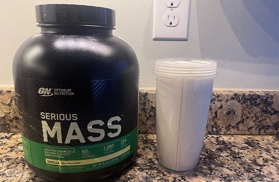 Side view of a shake next to a huge canister of Optimum Nutrition Serious Mass
