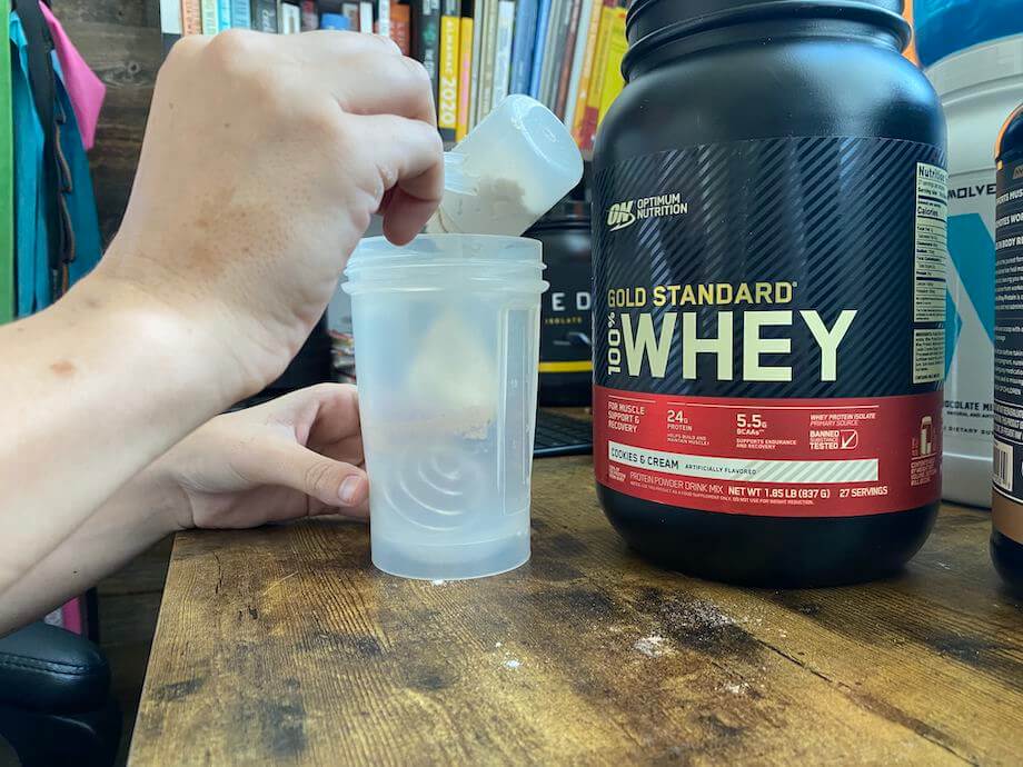 Person putting scoop of Optimum Nutrition Whey into shaker bottle