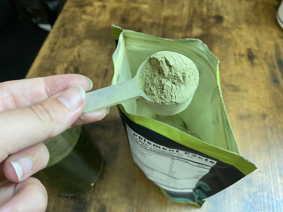 Close up of a scoop of Organifi Green Juice powder as it's lifted from the open bag.