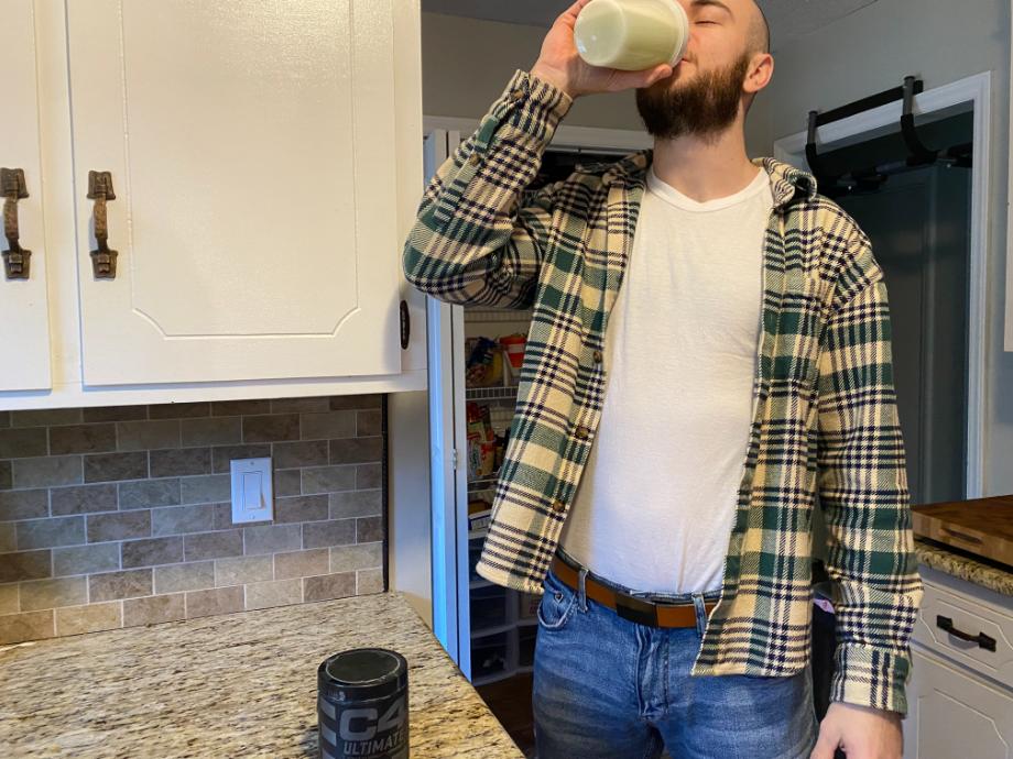 A person drinks a shaker cup of C4 Ultimate Pre-Workout in a kitchen with nice granite counters