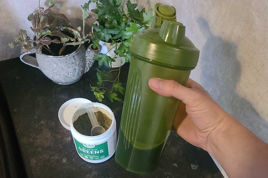 Person Holding Shaker Bottle With Nested Naturals Super Greens