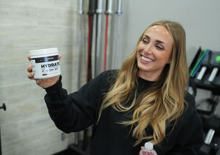 A smiling woman holds up a container of Transparent Labs Hydrate.