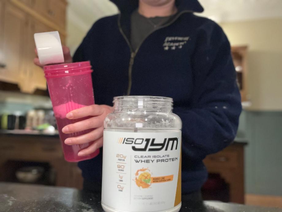 A person stands in a kitchen making a shake with ISO JYM 100% Whey Protein.