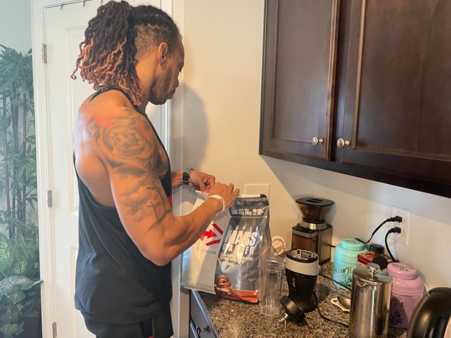 A person is shown opening a bag of Dymatize Super Mass Gainer.