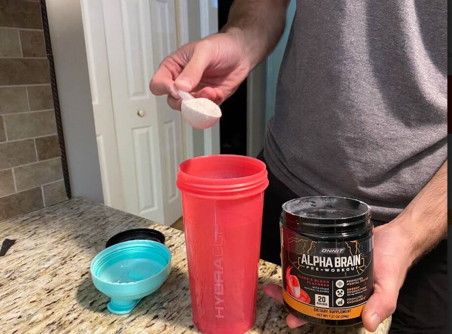 Person Scooping Alpha Brain Pre Workout Into Blender Cup