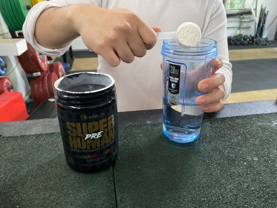 Person scooping Alpha Lion Superhuman Pre-workout into a shaker cup