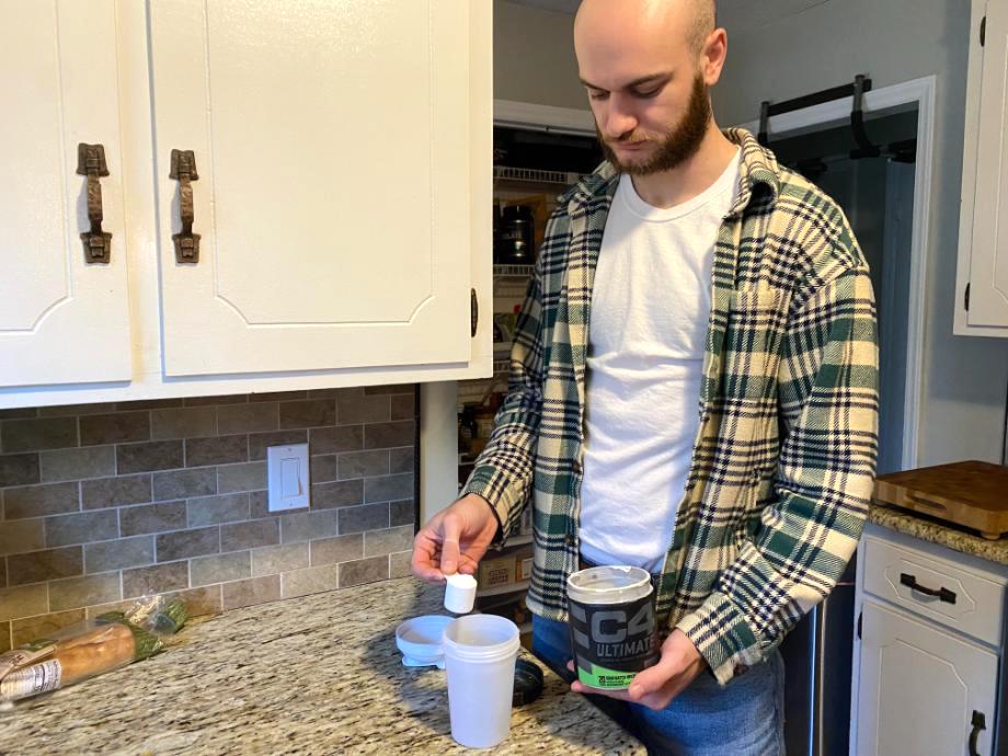 A person stands in a kitchen preparing a dose of C4 Ultimate Pre-Workout