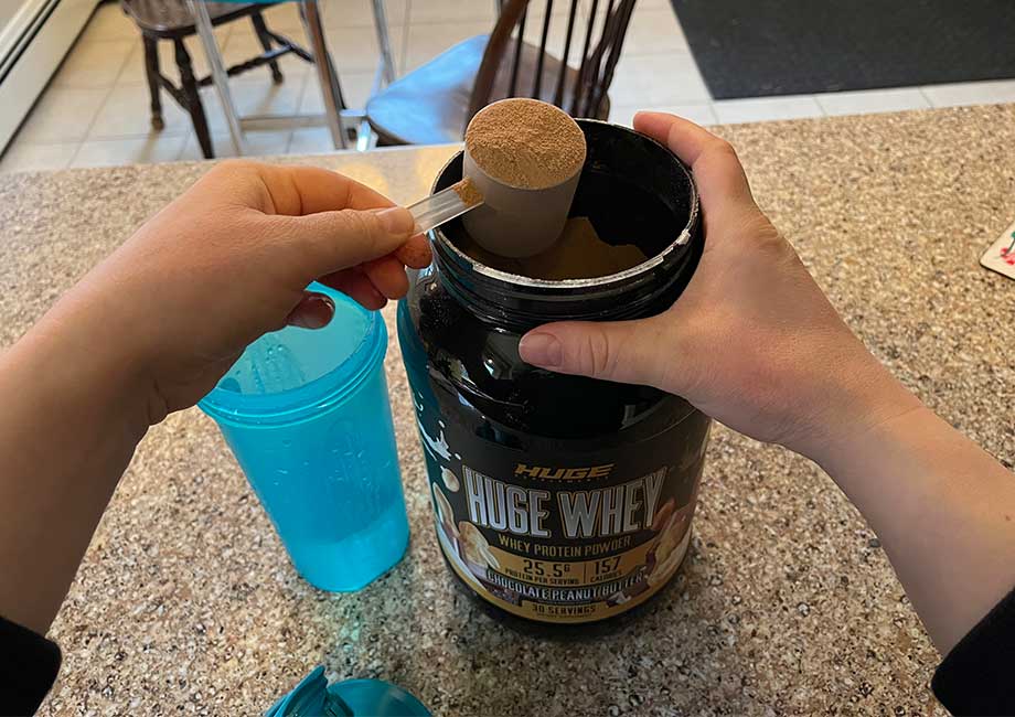 A person scoops Huge Whey Protein Powder out of the container