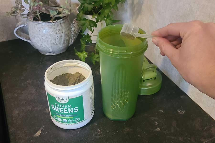 Person Scooping Nested Naturals Super Greens Into Shaker Bottle