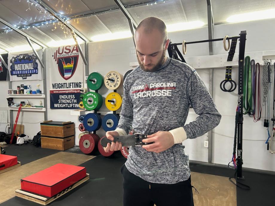 A person stands in a gym adjusting his Eleiko Weightlifting Belt.