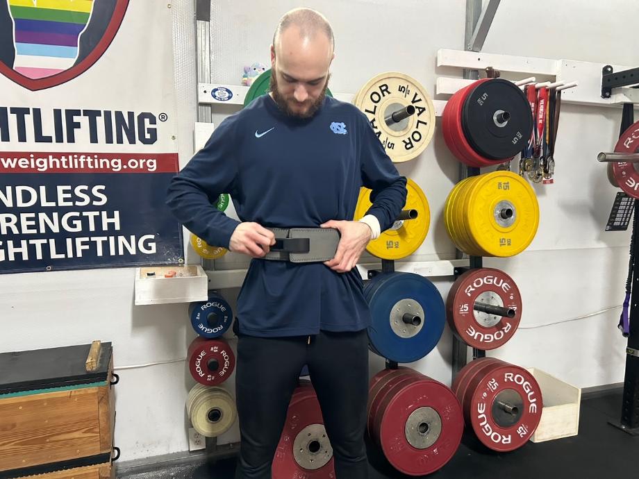 A person is shown tightening the Gymreapers Lever Belt while wearing it.