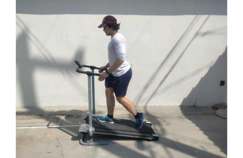 A person in workout clothes using a Sunny Health and Fitness manual treadmill
