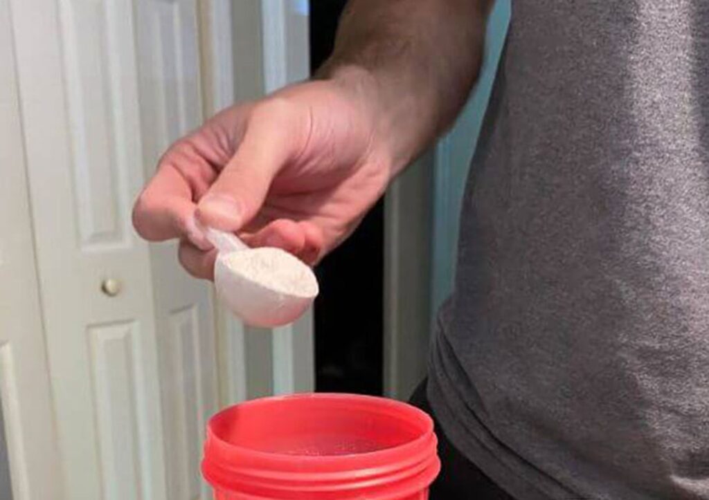 A person is shown pouring a scoop of Pre-Workout into a cup.