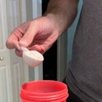 A person is shown pouring a scoop of Pre-Workout into a cup.