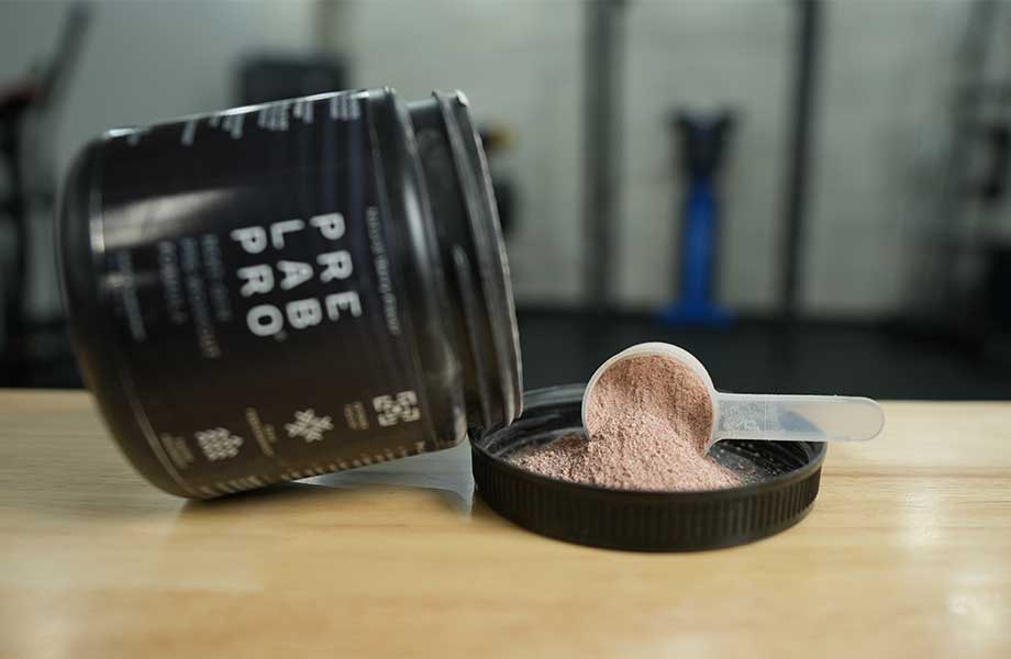 A scoop of Pre Lab Pro is shown dumped out in the up-turned lid, while the container lays on it's side