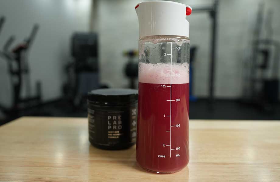 A deep red and frothy shake sits front and center, with a container of Pre Lab Pro pre-workout just behind the shake.