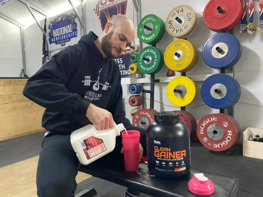 A man primes his shaker cup with milk before adding Rival Nutrition Clean Gainer.