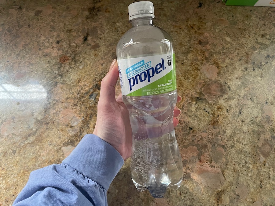 An image of a hand holding a bottle of Propel electrolyte water above a beige granite countertop