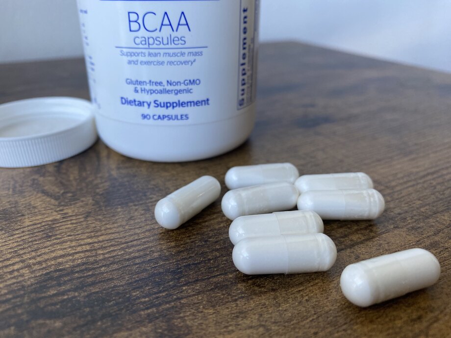 Some capsules are spilled on a table in front of a bottle of Pure Encapsulations BCAA Capsules.