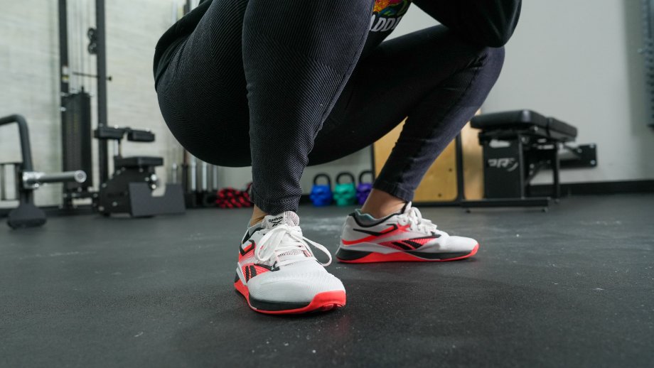 A person is shown doing squats while wearing Reebok Nano X4 cross-training shoes.