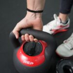 A hand holds a 16kg REP Fitness Adjustable Kettlebell.