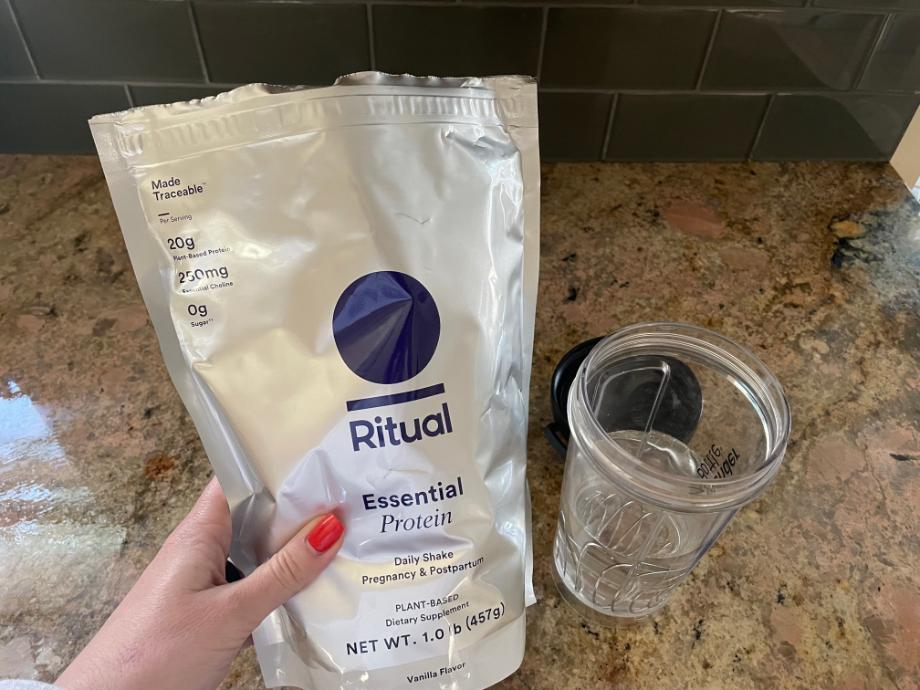 A hand holds a bag of Ritual Pregnancy Protein near a glass of water.