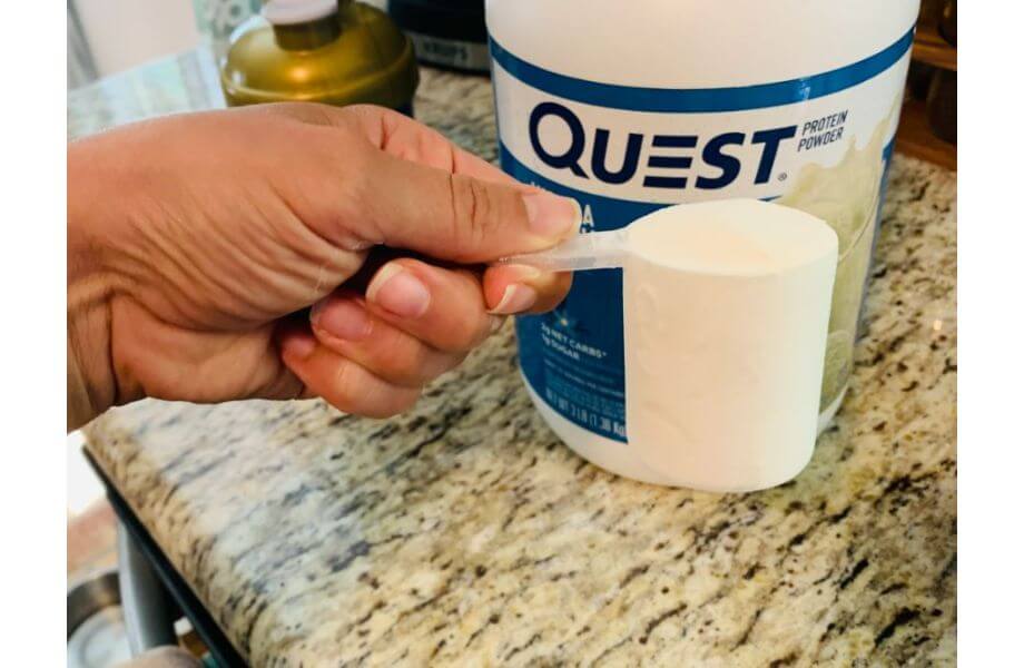 hand holding scoop in front of quest nutrition powder