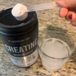 A person lifts a scoop of Jacked Factory Creatine from the container.