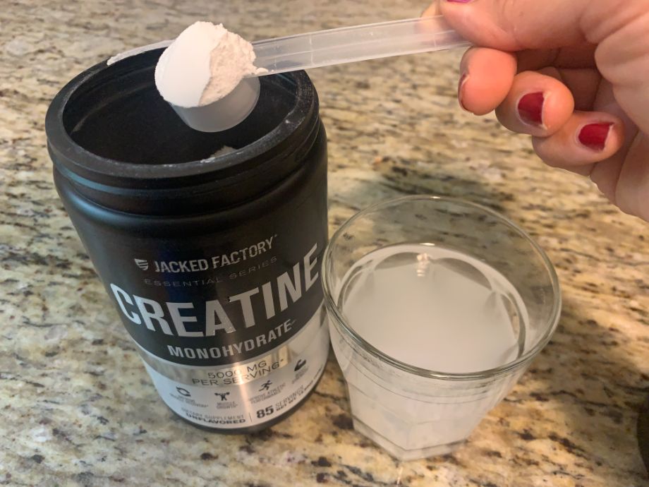 A person lifts a scoop of Jacked Factory Creatine from the container.