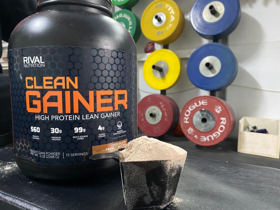A close-up view of a huge overflowing scoop of Rival Nutrition Clean Gainer, with the container towering over.