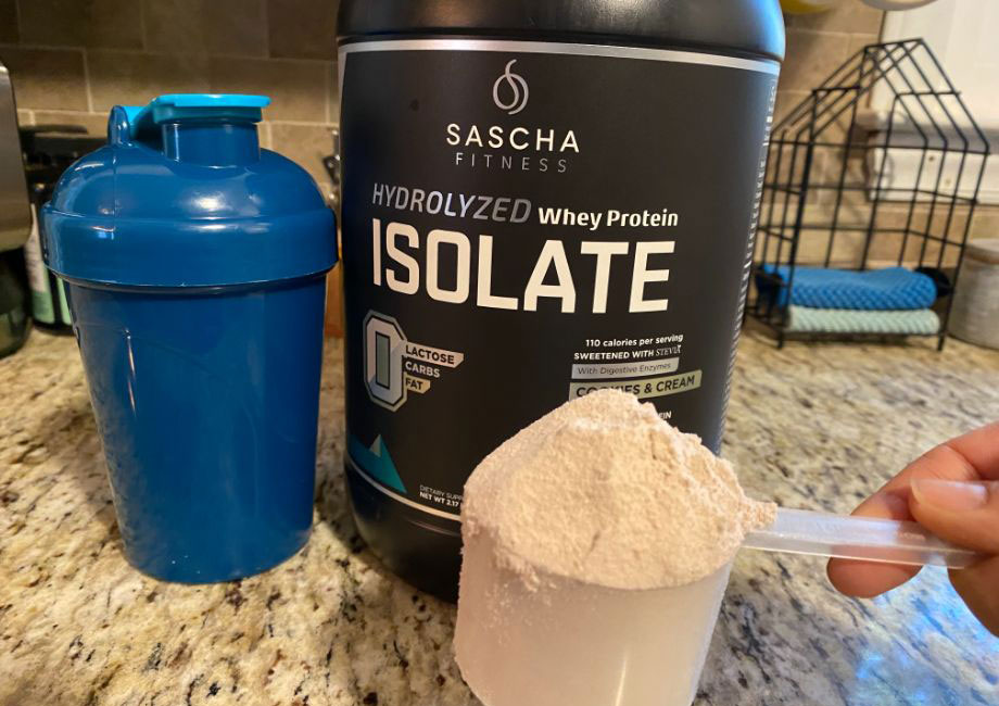 Scoop of Sascha fitness hydrolyzed whey protein powder with container and shaker bottle
